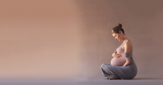 Young healthy pregnant woman doing yoga exercises and meditating at home. Health care, mindfulness, relaxation and wellness concept. 
