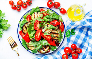 Grilled vegetables salad with paprika, zucchini, eggplant, tomatoes and spinach on plate, white table background, top view