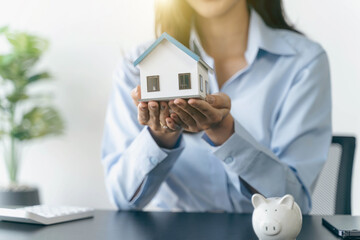 Businesswoman holding a house model.House on Hand with piggy bank.Real estate,Property insurance and security concept.Savings and finance concept.