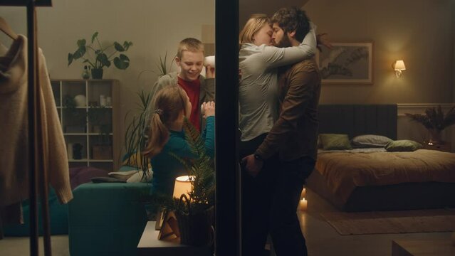 Two funny children interested about happening in neighbor apartment, eavesdrop through wall using glass cups. Passionate neighbor couple hot kiss and go to the bed. Neighbourhood concept. Static shot.