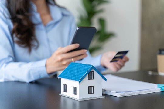 House model with woman holding credit card and mobile phone on the table.Property purchase idea, Interest rate for housing, Business and Financial for residence, Money saving for home concept.