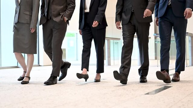 Video of a team of cool Japanese (Asian) businessmen in suits dashing around with office in the background, walking feet without full face.