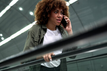 Young afro woman moving on escalator in underground tube and talking on mobile phone