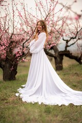 Woman peach blossom. Happy curly woman in white dress walking in the garden of blossoming peach trees in spring