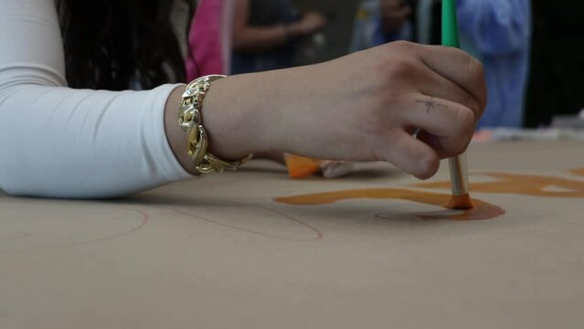 Slow motion close-up shot of a woman patining orange paint onto paper