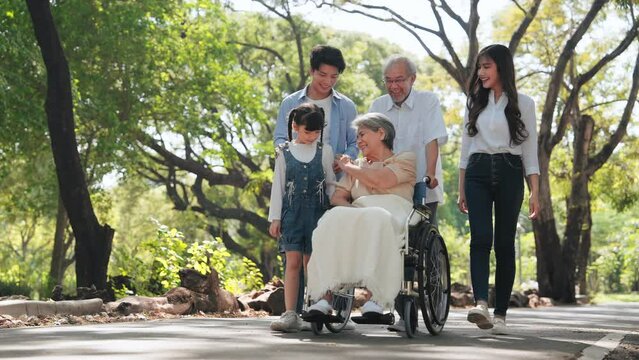 Happy Asian senior woman sitting on wheelchair in the park and take care by big family on weekends holiday