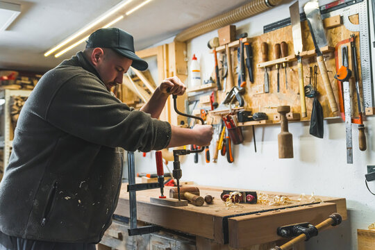 male carpenter using an old brace and creating a hole in a wooden plank, medium shot. High quality photo
