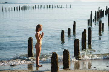 A young beautiful girl meditates with folded hands in namaste, on the beach, against the backdrop of the ocean. 