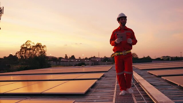 Asian worker or engineer walking and inspecting solar panels on rooftop during sunset time, Sustainable life concept