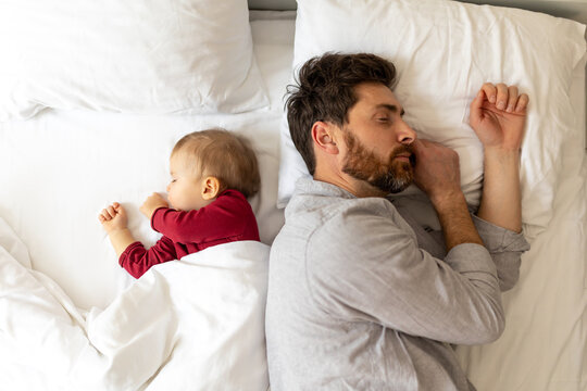 Father and little baby sleeping together in bed.