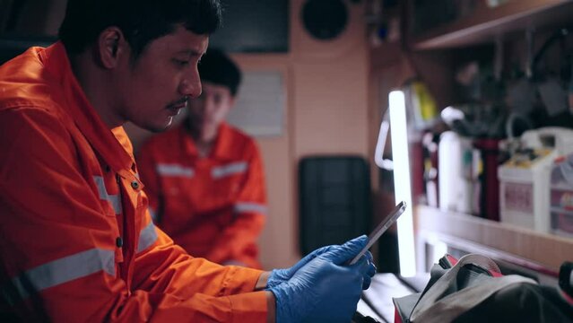 Emergency medical technician (EMT) Asian woman or paramedic using tablet and sitting in ambulance car while the car was going to the emergency location and turned on the siren light