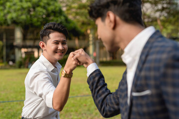 A young asian man fist bumps with an indian co-worker while outside the office.