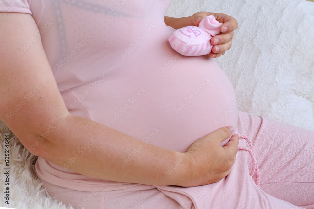 Poster middle-aged pregnant woman in pink t-shirt holding her belly, waiting for newborn, concept of pregnancy reproduction, in vitro fertilization, planning late pregnancy after 40 years, selective focus