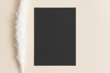 Black invitation card mockup with a pampas on the beige table. 5x7 ratio, similar to A6, A5.