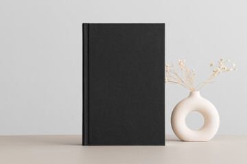 Black book mockup with a gypsophila decoration on the beige table.