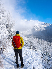 a man in a yellow jacket is standing on the tourist trail and looking at the magnificent view. Mountainet a snowy mountain in a sunny winter day. Tatras ,Slovakia.