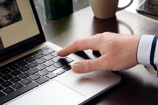A man presses the enter key on a modern laptop, against the background of a cup of coffee and a smartphone