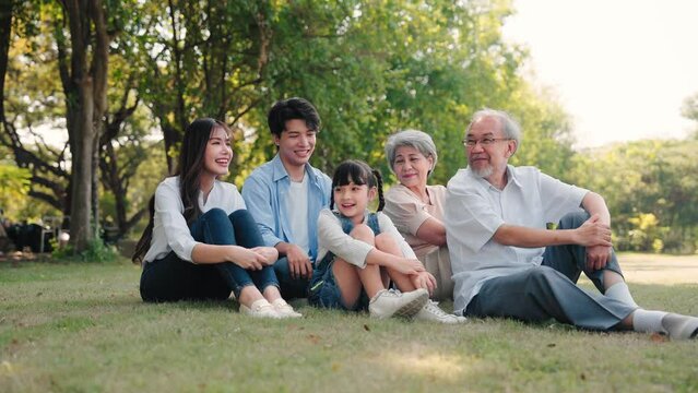 Happy Big Asian family talking together and sitting on sward grass