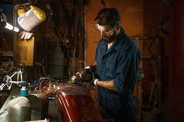 Fototapeta na wymiar Repairman grinding motorcycle body part from old paint using stripping machine