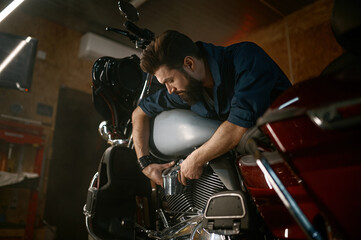 Fototapeta na wymiar Male mechanic working in garage and repairing custom motorcycle