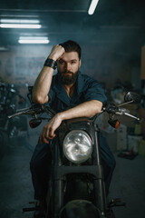 Portrait of brutal man mechanic sitting on repaired motorcycle