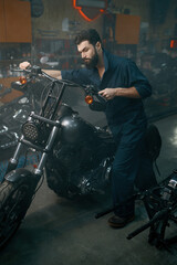 Fototapeta na wymiar Auto mechanic pushing motorcycle on repair stand in workshop garage
