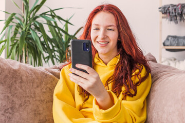 Smiling teenage girl sitting on couch and looking at phone screen