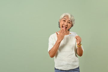 Excited senior woman with credit card isolated on green pastel background. Shopping and payment concept