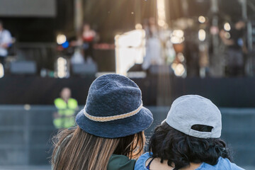 Friends with hats statying in front of a summer music festival stage. Waiting for the concert to...