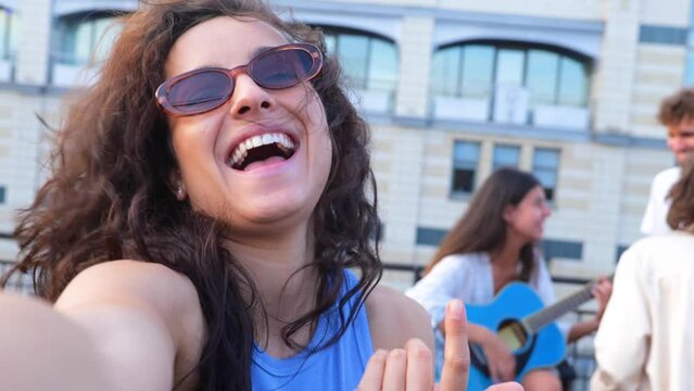 Happy young people dancing while having open air party on the rooftop. Young woman playing guitar. Clubbing, fun, open party concept. Real time