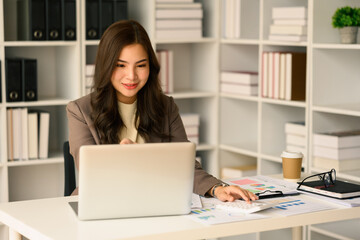 Photo of female analyst looking at laptop using calculator, checking marketing research results or statistics data