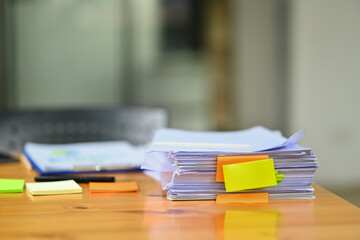 Pile of documents with colorful sticky notes on wooden office desk. Organized document management system concept