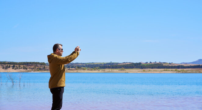 a man taking a picture with a mobile phone on a lake shore