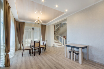 Luxury interior design of a country house. Windows with beautiful curtains, a dining table, a wide passage to the hall with a white staircase.