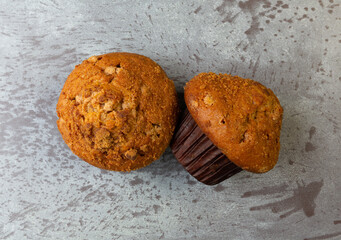 Top view of two freshly baked cinnamon muffins with one on its side on a gray mottled background.