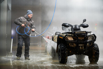 Full length of man cleaning quad bike with high pressure water sprayer at self-service car washing...