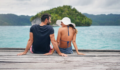 Vacation, ocean and back of couple together on deck, dock or sitting on boardwalk to relax and enjoy the sea, water or landscape. People, man and woman on holiday, summer travel or date in nature