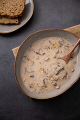 Wooden cutting board with a bowl filled with a creamy mushroom soup and a slice of bread beside it