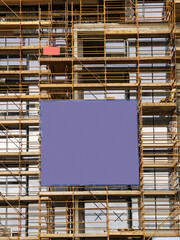 Side of a new building in scaffolding and safety nets and blue color banner. Construction site safety measures. Developing commercial or residential property. Growth concept.