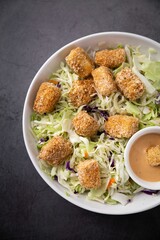 White bowl filled with a variety of colorful foods, including a dipping sauce and a side salad