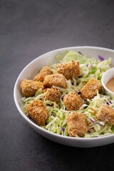 White bowl filled with a variety of colorful foods, including a dipping sauce and a side salad