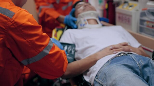 Asian emergency medical technician (EMT) or paramedic measuring blood pressure to a patient in ambulance car