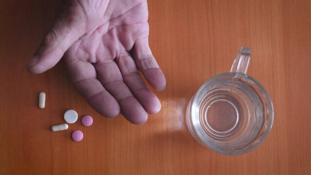 a handful of pills in the palm of an elderly man, a pensioner takes medicine by taking it from his hand and sipping water.top view.be healthy concept
