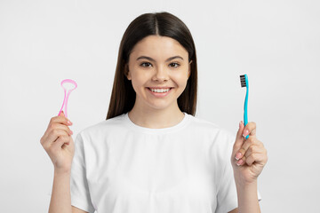 Portrait of smiling  teenage girl holding toothbrush and tongue cleaner looking at camera isolated...