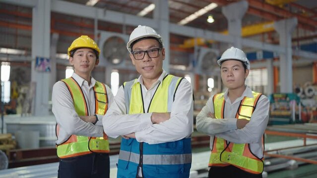 Close up smiling face team of asian machine technicians men in safety uniform standing with arms crossed looking at camera at industrial. Teamwork concept