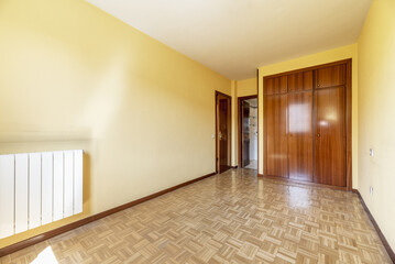 An empty room with a built-in wardrobe with three-section varnished sapele doors