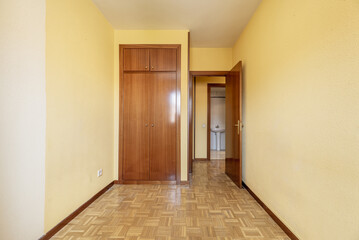 An empty room with a built-in wardrobe with two-section varnished sapele doors