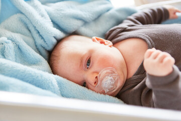 Cute baby with pacifier lies peacefully in bed