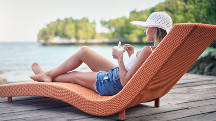 Chair, ocean and woman relax with a drink outdoor on a vacation, holiday or adventure in nature. Female person on tropical lounger, travel and deck with lake water in summer for zen, peace and calm