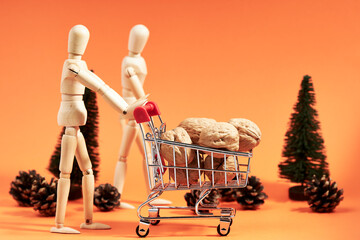 Couple of dummies pushing shopping cart with nuts next to pine trees on orange background